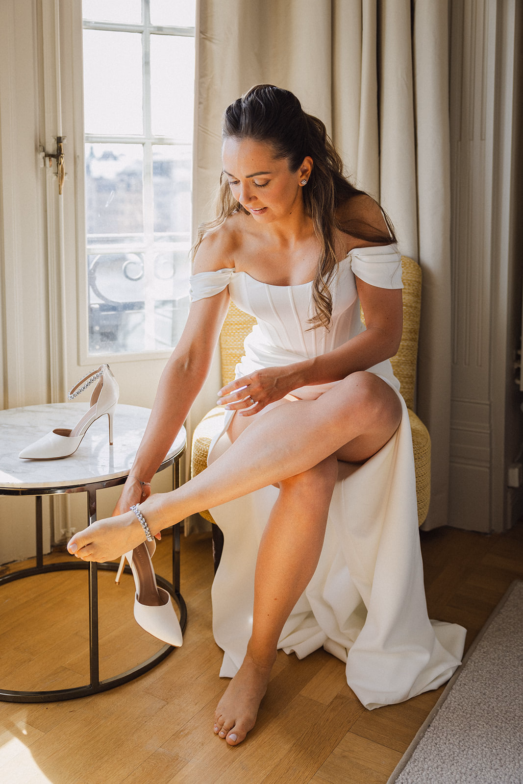 The bride putting on her shoes beside a window at Hotel Diplomat in Stockholm.