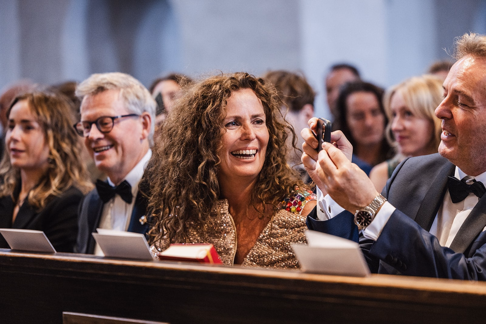 Wedding guests laughing together in a church pew before the ceremony.