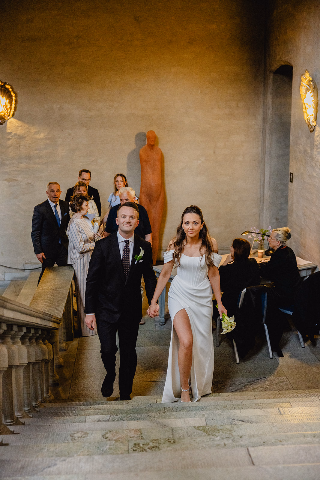 Gintare and Mikael climbing the stone stairs inside Stockholm City Hall with their guests behind them.