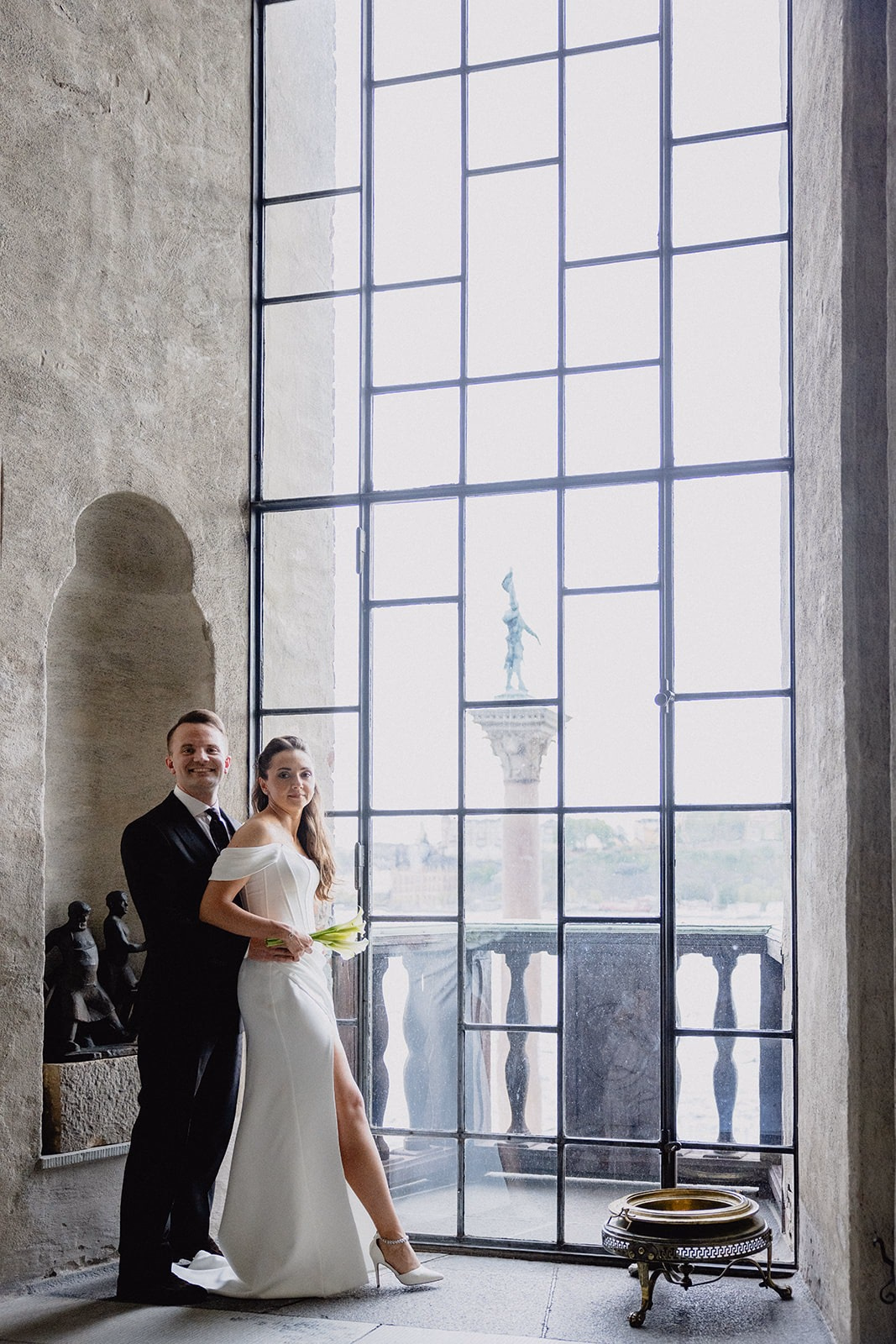Gintare and Mikael embracing beside the monumental window inside Stockholm City Hall.