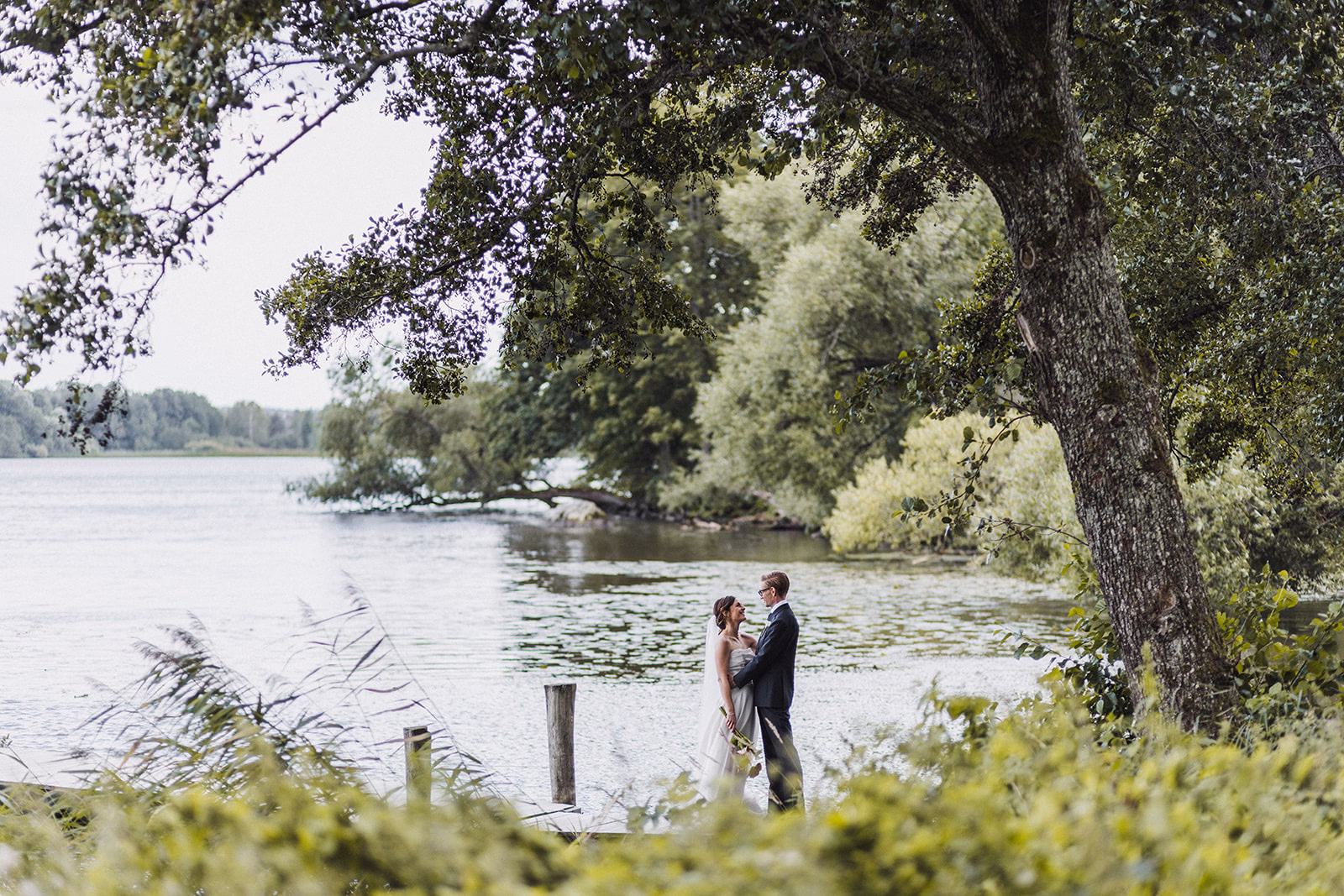 The newlyweds standing beneath a tree beside the lake in Strängnäs.