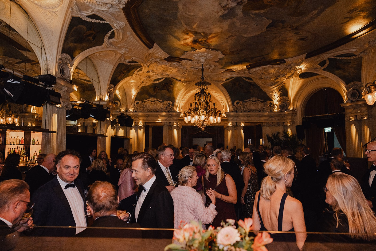 Wedding guests talking beneath the gilded ceiling at Café Opera.