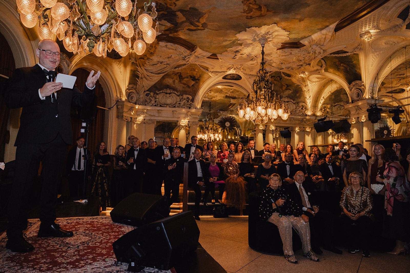 The newlyweds standing before their guests in the gilded hall at Café Opera.