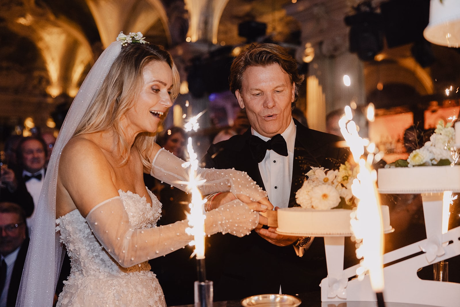 The newlyweds cutting their wedding cake beside indoor sparklers.
