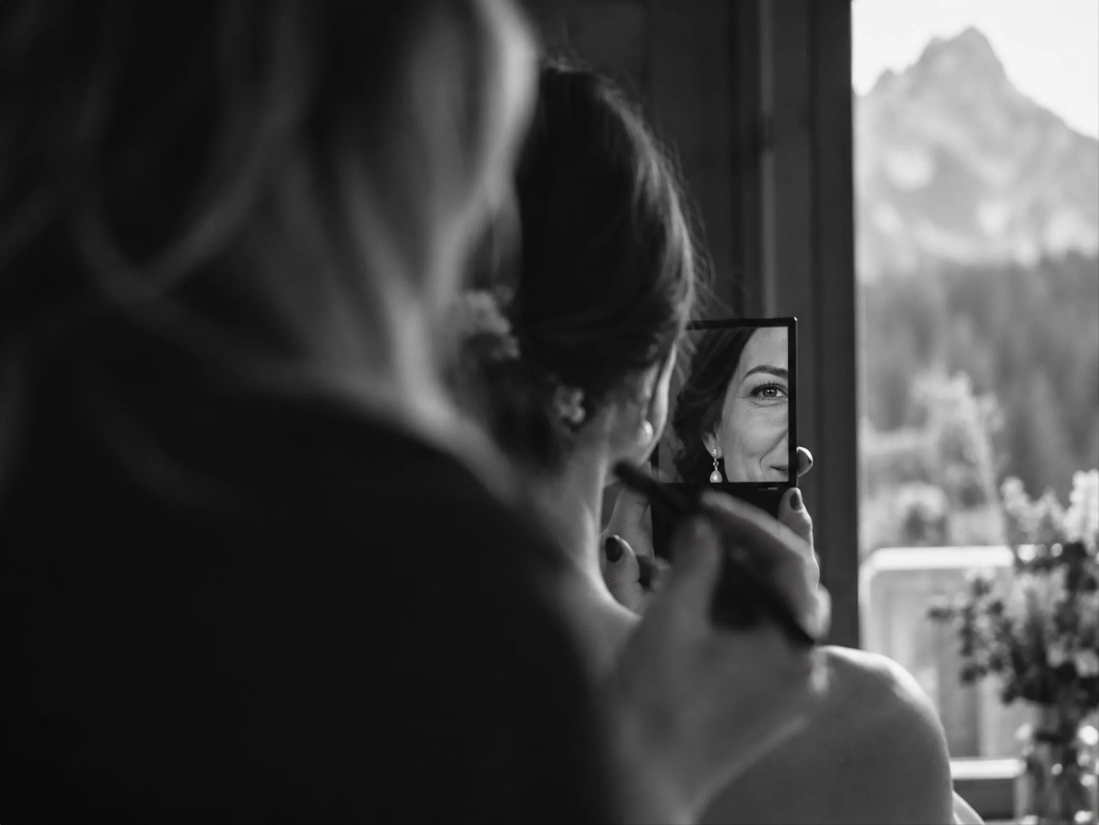 A bride checks her makeup beside a window overlooking the Dolomites mountains.