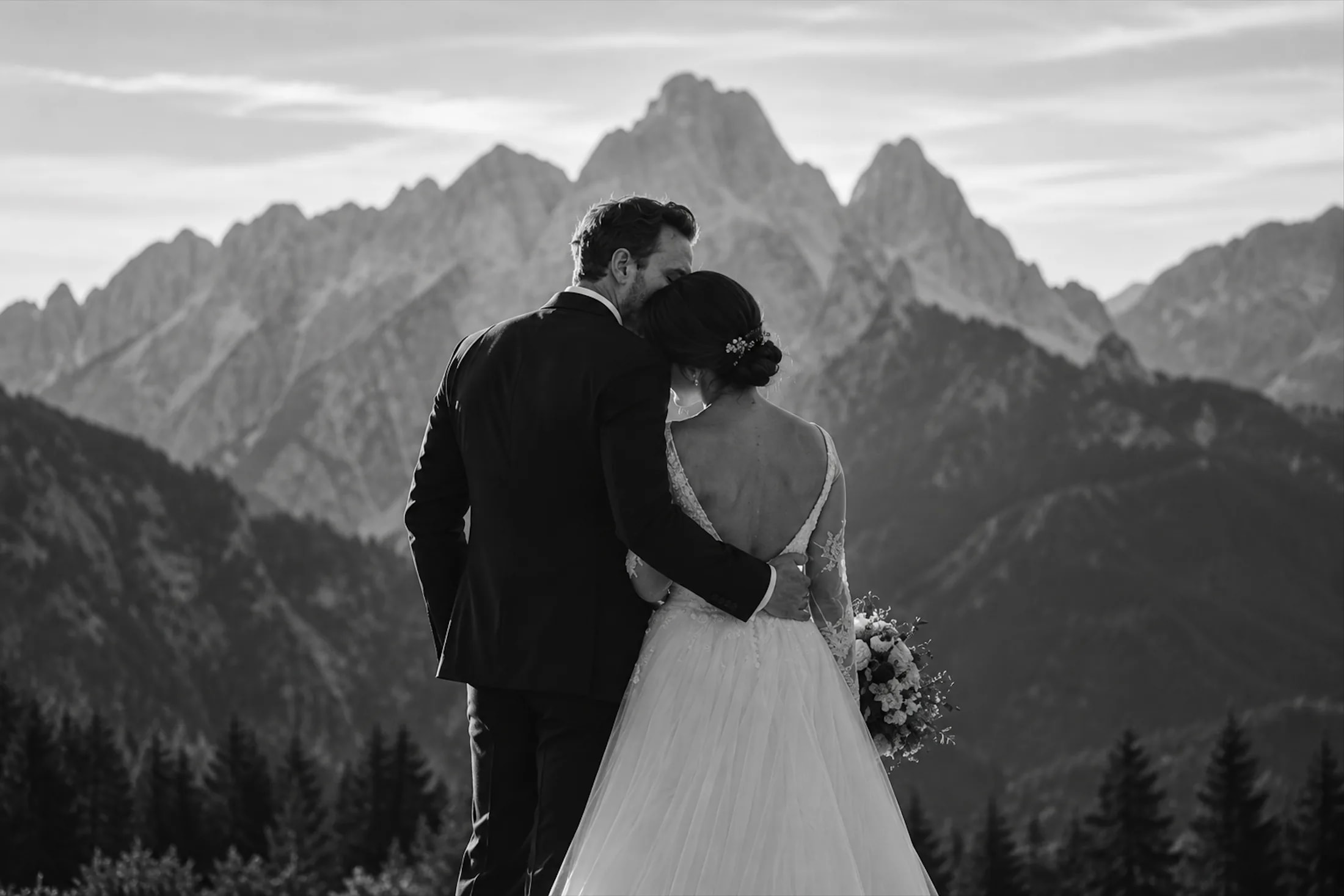 A bride and groom embrace with Dolomites mountain peaks behind them.