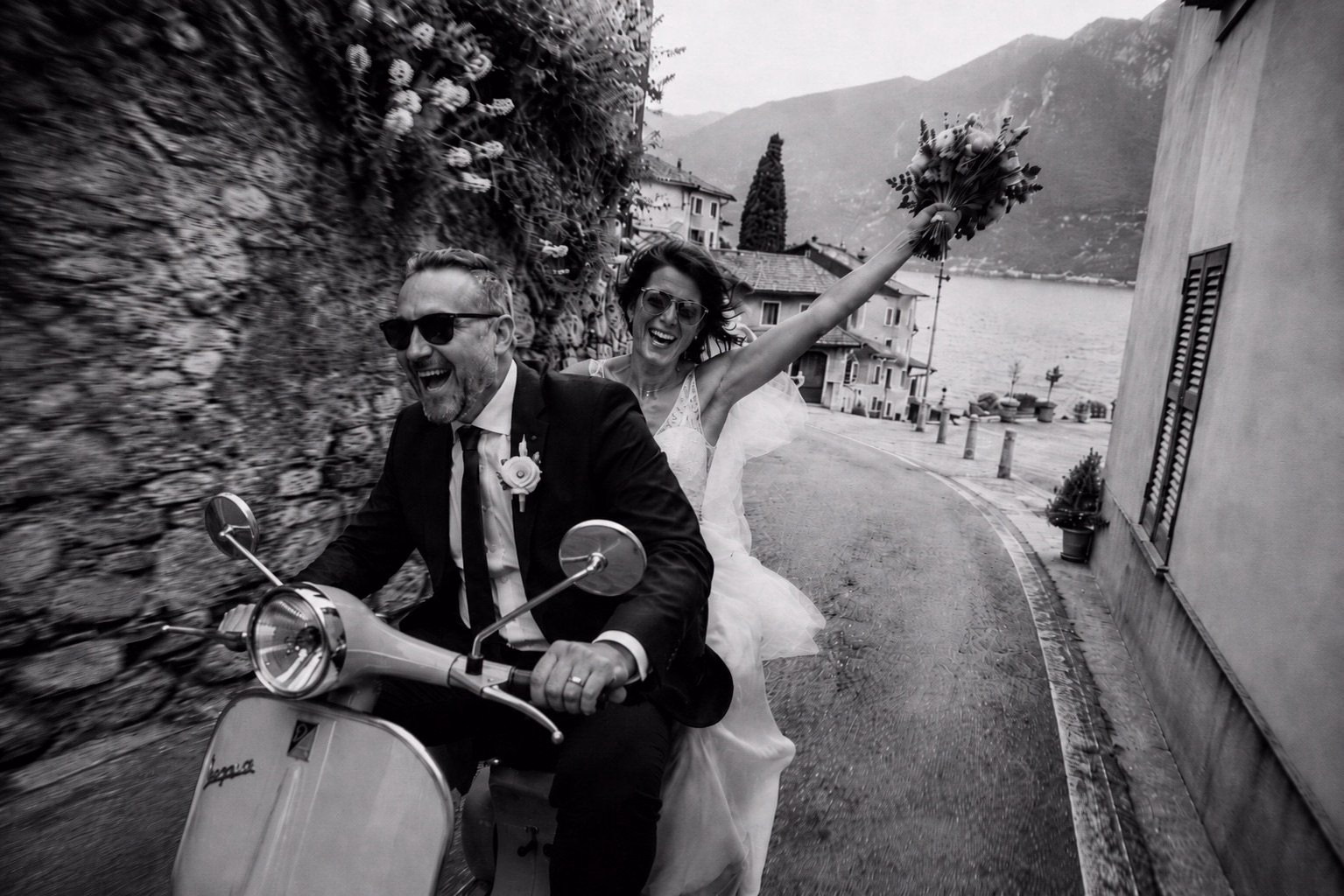 Gli sposi attraversano in Vespa un borgo sul lago.