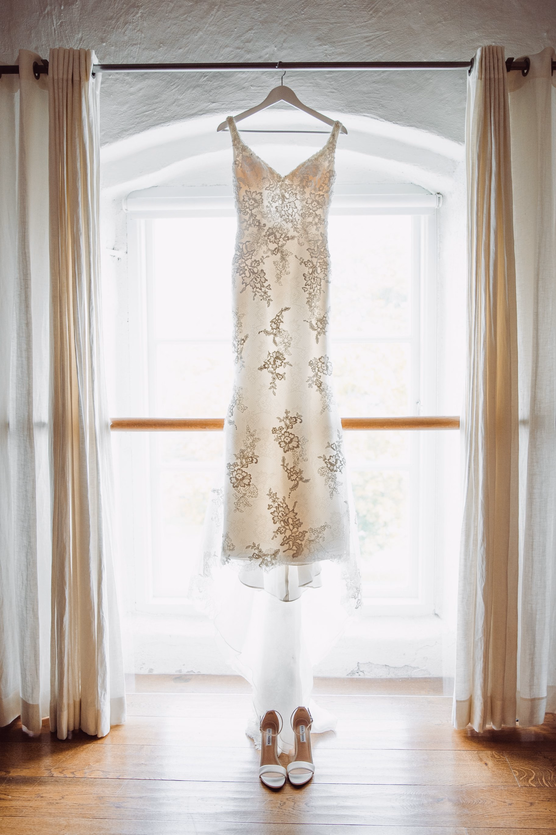 L’abito da sposa appeso davanti a una finestra sopra un paio di scarpe.