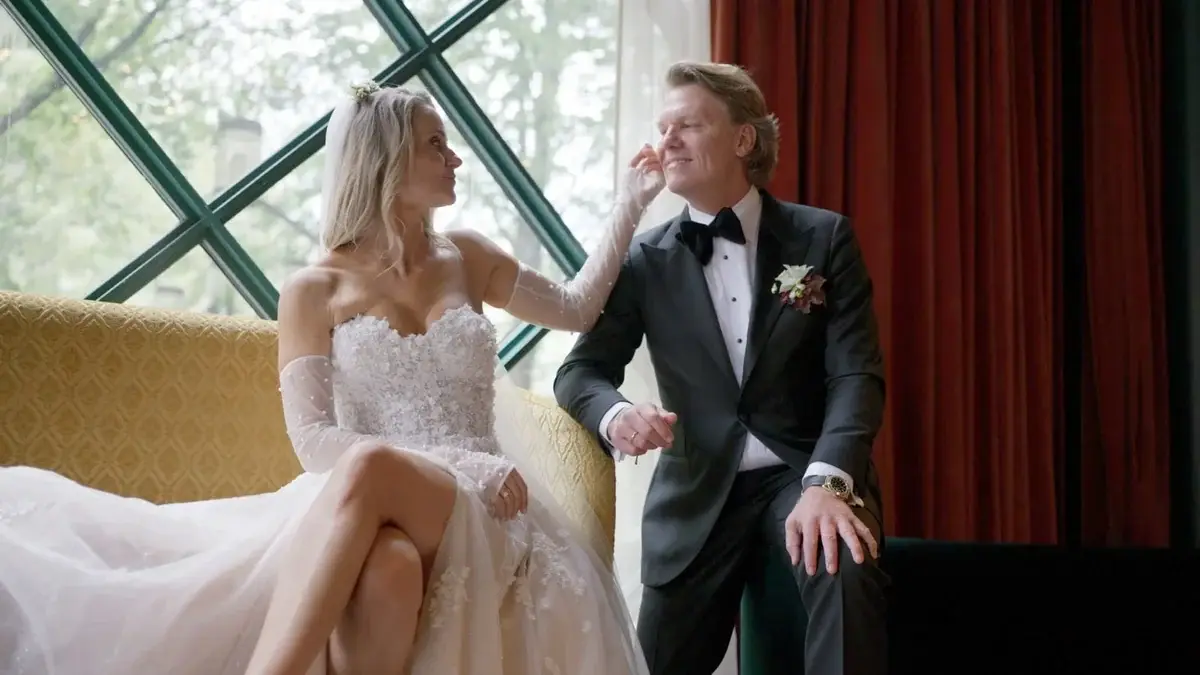Vanessa touching Jens’s face as they sit together beside an arched window at Café Opera.