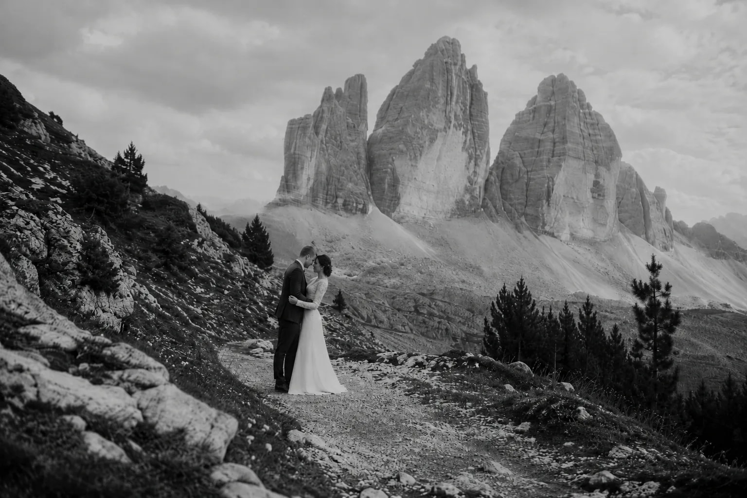 A bride and groom beneath Tre Cime di Lavaredo in a black-and-white Dolomites wedding portrait.