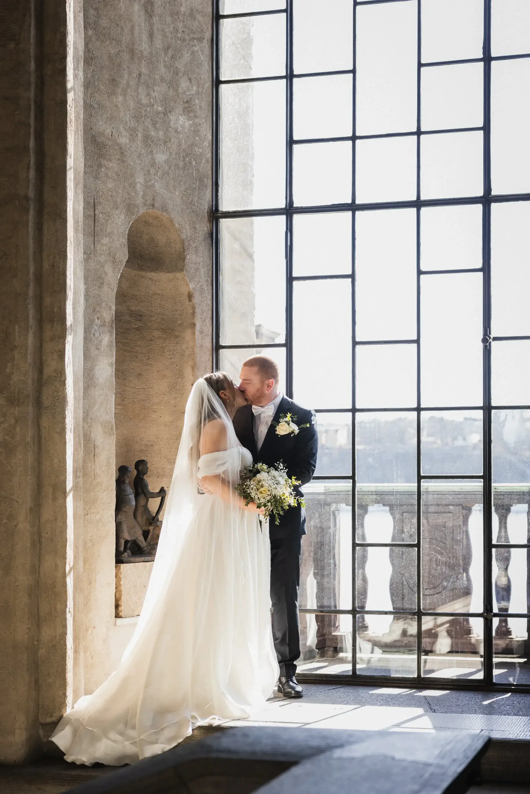 Couple embracing beside a tall window at Stockholm City Hall.