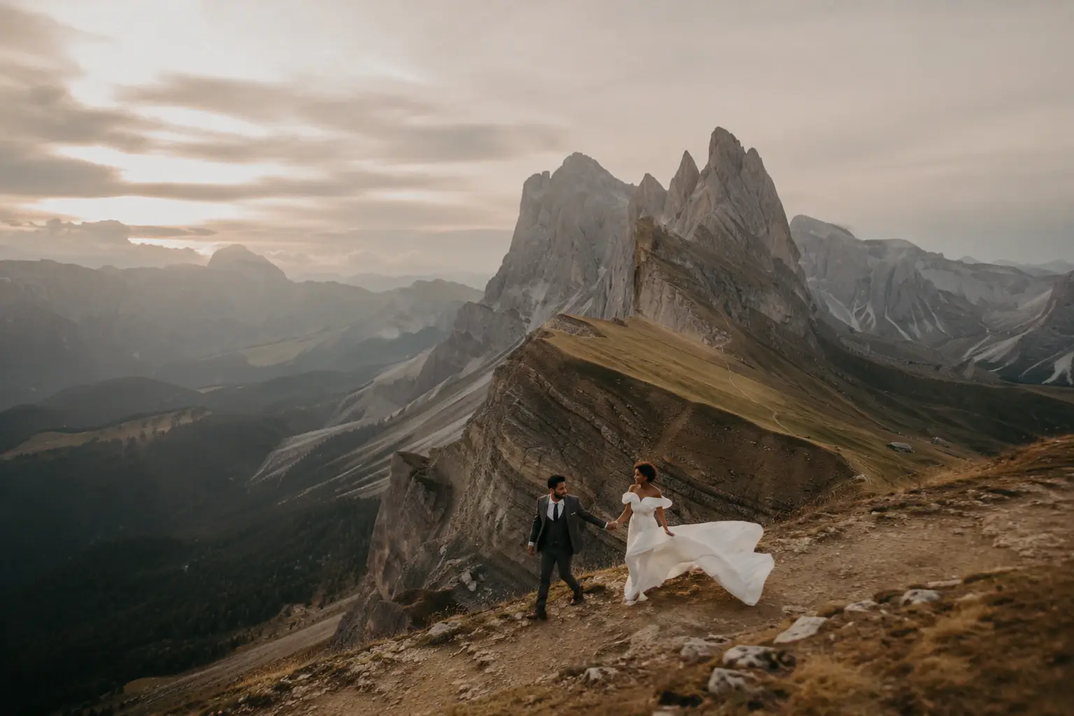 Bride and groom hiking through the Dolomites during a destination wedding portrait session with dramatic mountain peaks and flowing wedding dress.
