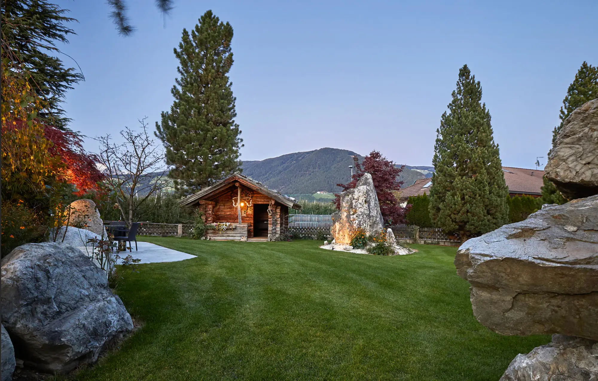 Garden and timber chalet surrounded by mountains.