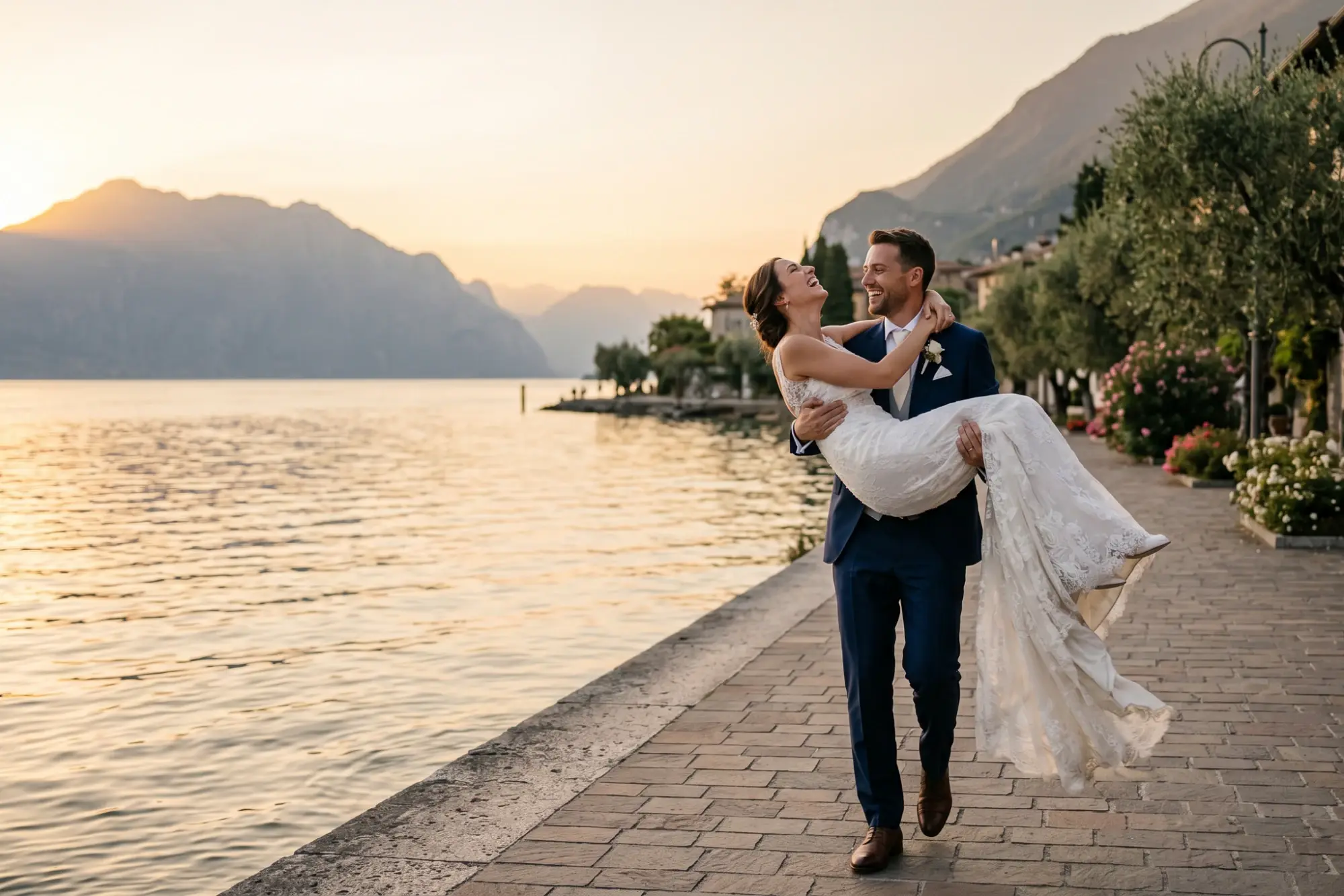 Alt text: Bride and groom walking along the waterfront at sunset during a Lake Garda wedding, with mountain views.