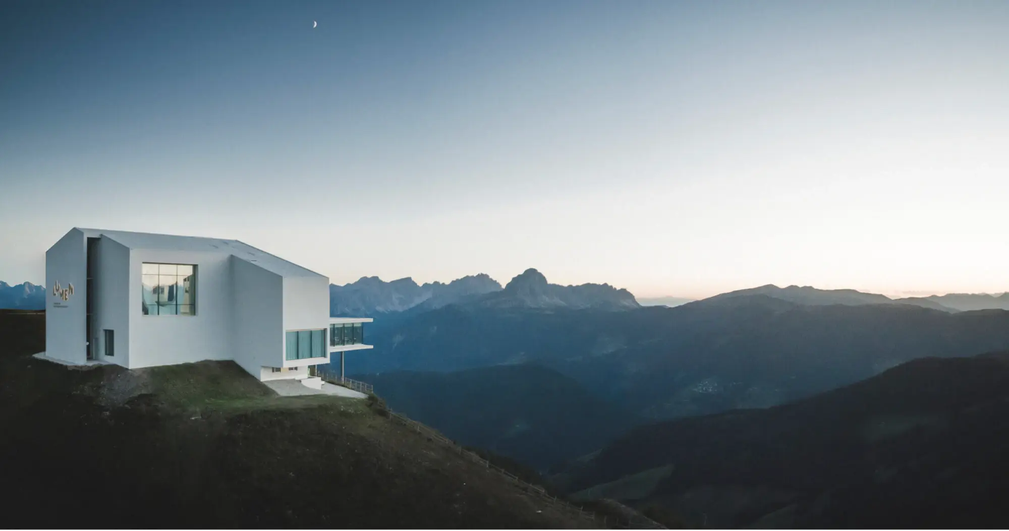 Modern white mountain lodge against a dark ridge.
