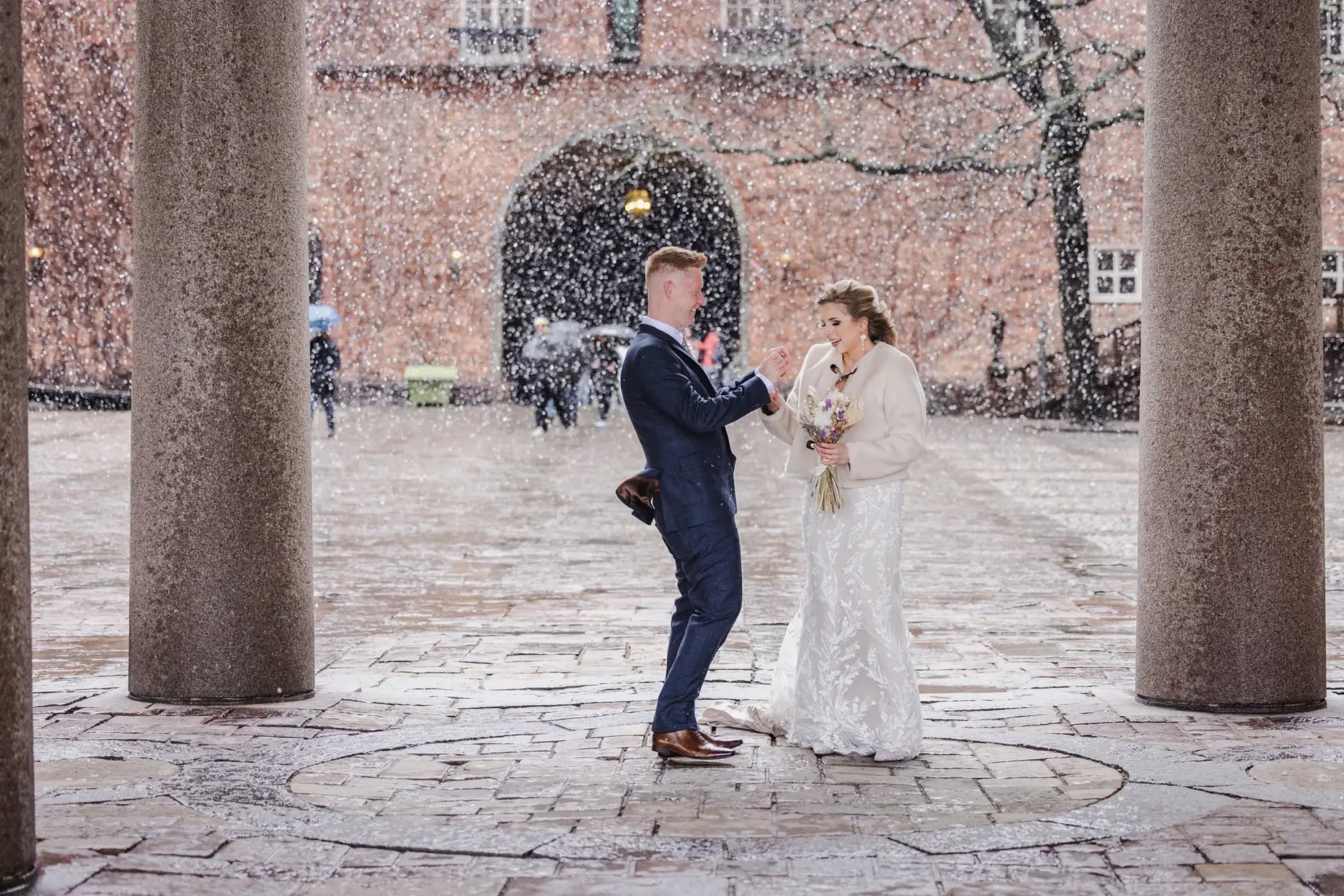 Newlyweds opening champagne in the snow at Stockholm City Hall.