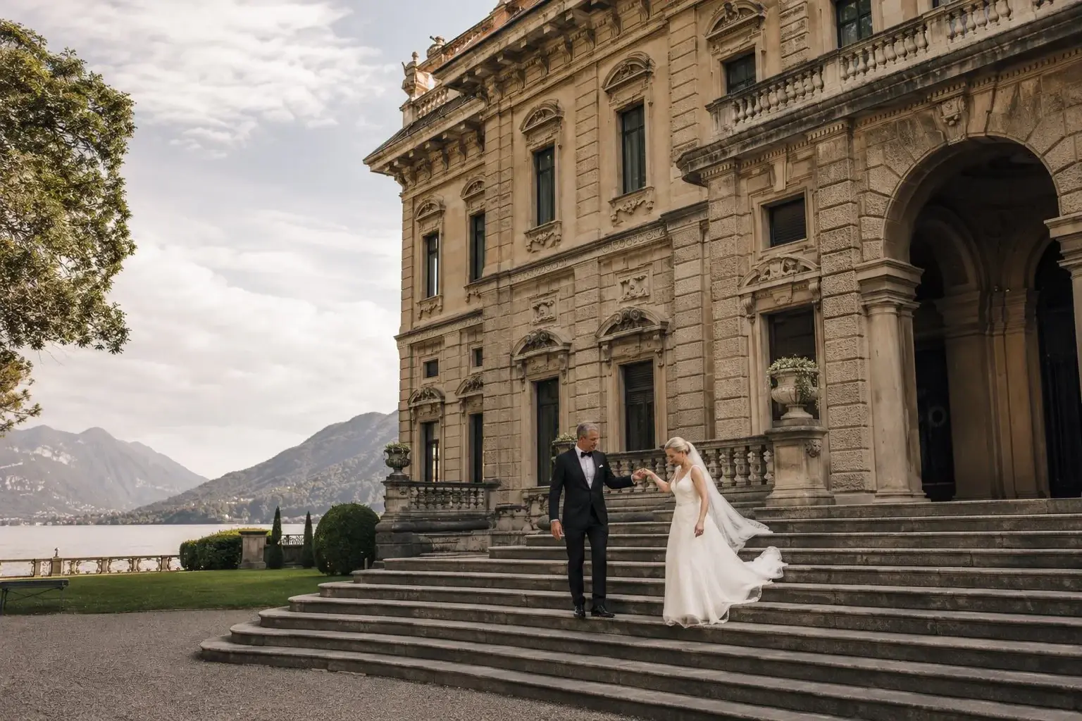 Bride and a formally dressed man on the steps of a lakeside villa.