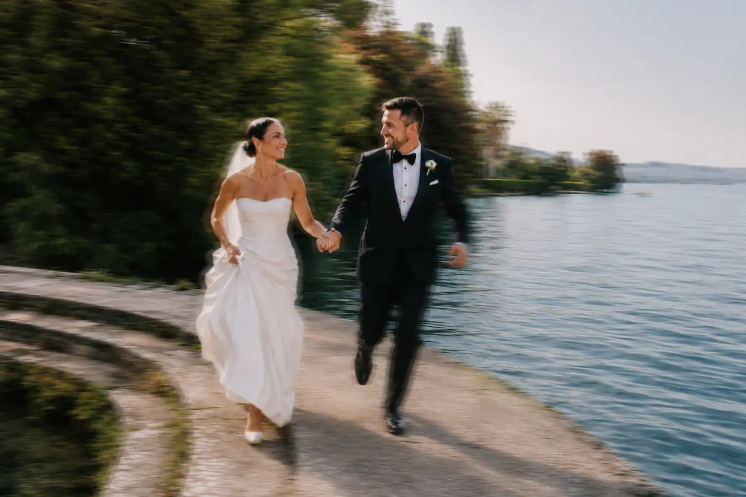 Newlyweds running together beside a lake.